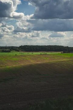 Thick clouds over green fields. The highway is far beyond the field Stock Photos