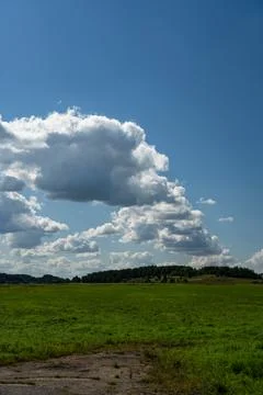 Thick clouds over green fields. The highway is far beyond the field Stock Photos