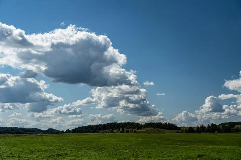 Thick clouds over green fields. The highway is far beyond the field Stock Photos