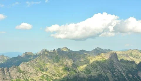 Thick cumulus clouds casting shadows float over the spiky mountain peaks on.. Stock Photos