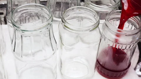 Thick dark red syrup flows smoothly from a transparent jug into a clean jar.  Видео 337678523