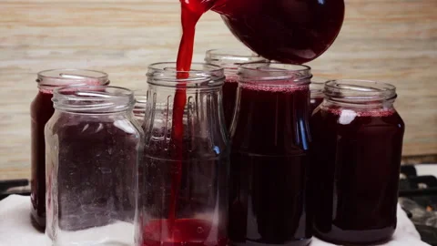 Thick dark red syrup flows smoothly from a transparent jug into a clean jar.  Stockbeeldmateriaal 337679966