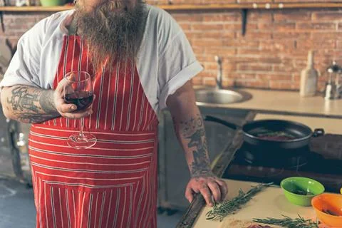 Thick guy drinking wine while cooking Stock Photos