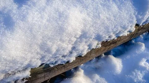 A thick layer of fresh white snow covers a rustic wooden beam on a sunny wi.. Stock Photos
