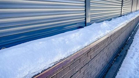 A thick layer of fresh white snow lying on a brown brick wall next to blue .. Stock Photos