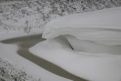 A thick layer of snow overhanging an almost frozen ditch Stock Photos
