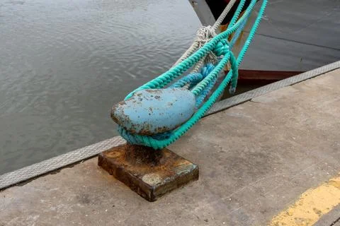 Thick nautical ropes secured to a weathered bollard on a concrete pier by t.. Stock Photos
