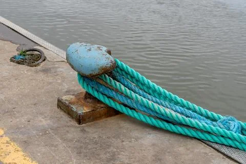 Thick nautical ropes secured to a weathered bollard on a concrete pier by t.. Stock Photos