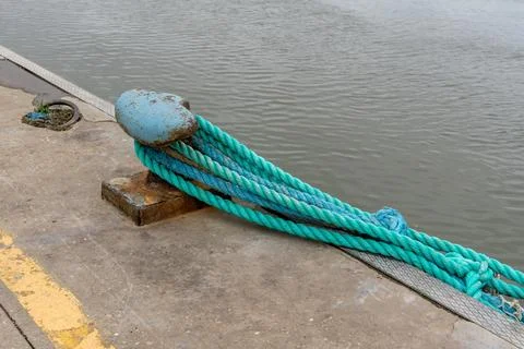 Thick nautical ropes secured to a weathered bollard on a concrete pier by t.. Stock Photos