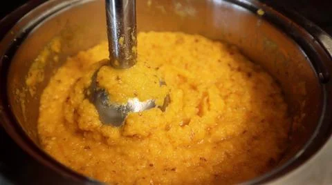 Thick orange vegetable puree is being blended in a metal pot. Stock Photos