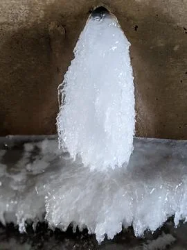 Thick Pillar of Solid Ice Frozen to a Dark Concrete Wall 스톡 사진