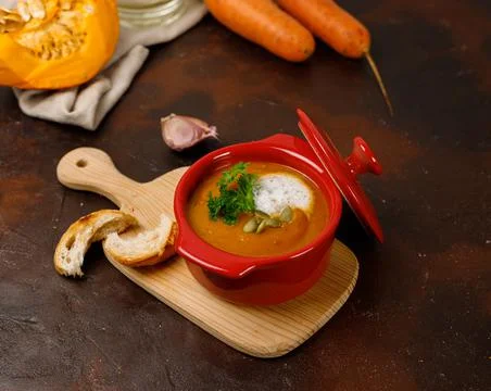 Thick pumpkin soup in a ceramic red bowl. On a light wooden table with Stock Photos
