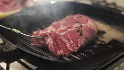 Thick raw steak seared on a hot cast iron grill pan with steam rising Stock Footage 340563279