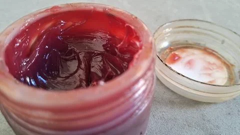 Thick red industrial grease inside a small open plastic jar Stock Photos