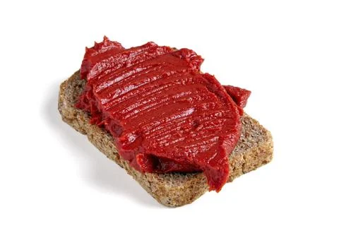 Thick red tomato paste spread thickly on a piece of coarse black bread. Stock Photos