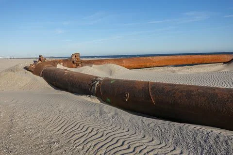 A thick rusty pipeline making a right angle turn on a sandy beach  Stock Photos