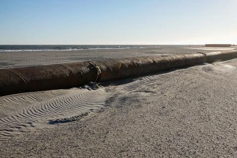 A thick rusty pipeline on a sandy beach near the ocean Stock Photos