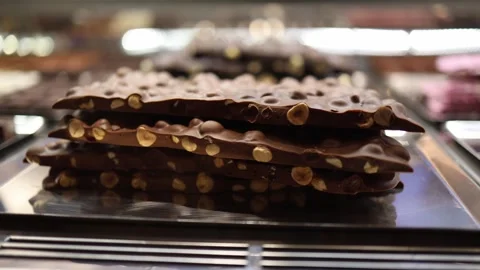 Thick slabs of artisan chocolate loaded with roasted hazelnuts stacked on a meta Stock Footage 310053368