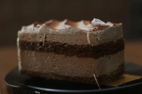 A thick slice of layered chocolate cake sits on a dark plate, with creamy fro 库存照片