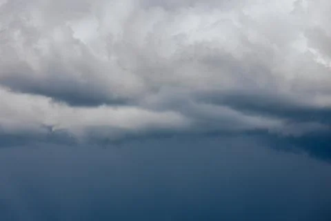 Thick storm clouds stretch across the sky with a visible curtain of rain falling Stock Photos
