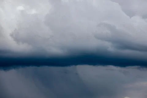 Thick storm clouds stretch across the sky with a visible curtain of rain falling Stock Photos