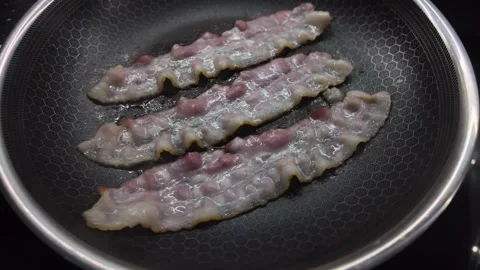 Thick strips of streaky bacon sizzling vigorously in a textured non-stick f.. Stock Footage 318828826