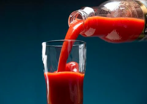 Thick tomato juice pours from a bottle into a glass Stock Photos