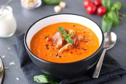 Thick tomato soup with basil and fried bacon in a black ceramic bowl. Stock Photos