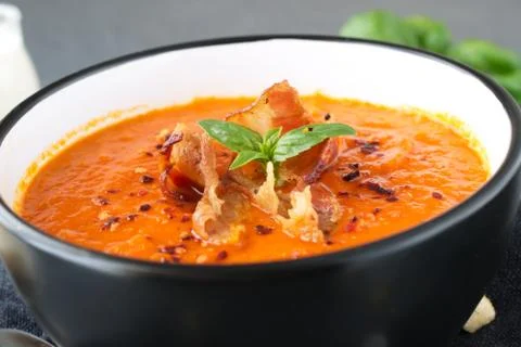 Thick tomato soup with basil and fried bacon in a black ceramic bowl. Stock Photos