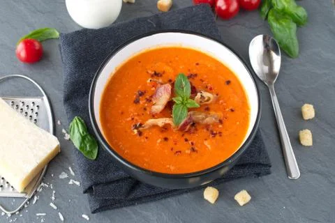 Thick tomato soup with basil and fried bacon in a black ceramic bowl. Stock Photos