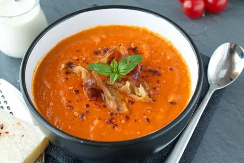 Thick tomato soup with basil and fried bacon in a black ceramic bowl. Stock Photos