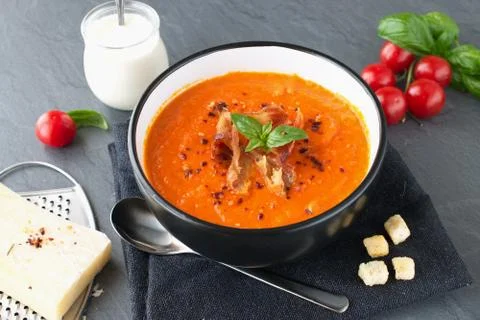 Thick tomato soup with basil and fried bacon in a black ceramic bowl. Stock Photos
