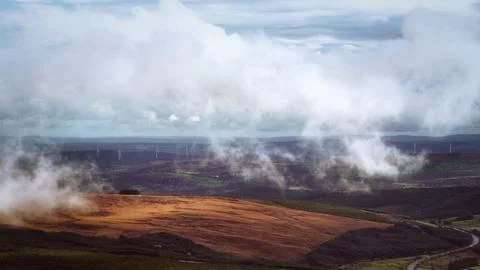 Thick white clouds hang low over a vast, undulating landscape. Stock Photos