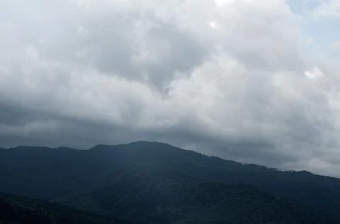 Thick white clouds over mountains covered with green forest. green trees in a Foto stock