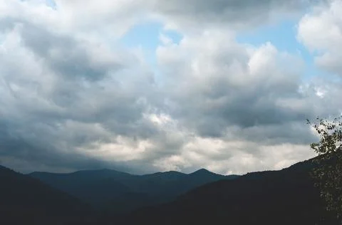 Thick white clouds over mountains covered with green forest. green trees in a Stock Photos