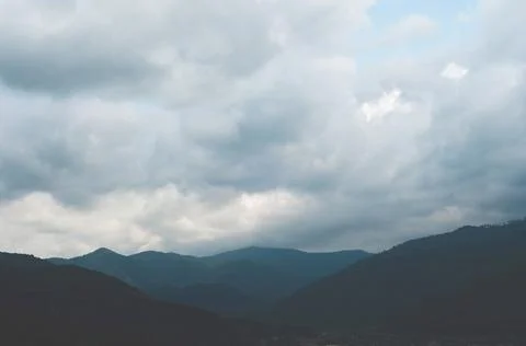 Thick white clouds over mountains covered with green forest. green trees in a Stock Photos