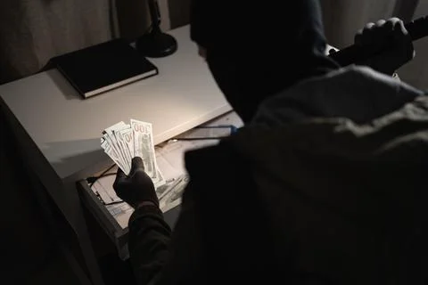 Thief in black balaclava into apartment using flashlight searching money, banner Фото