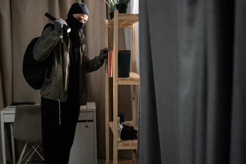 Thief in black balaclava. Robber with flashlight entering a house for stealing Stock Photos