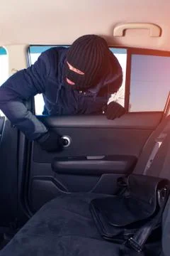 Thief in black robbery mask stealing bag from car Stock Photos