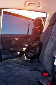 Thief in black robbery mask stealing bag from car Stock Photos