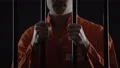 Thief in jail feeling sincere regret of crime, holding prison bars in desperate 4k or 4k+ Resolution