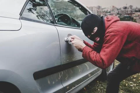 Thief looking inside a car window ready to steal something. Criminal in black Foto stock