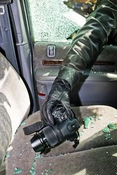 A thief steals a camera from a car through a broken side window. Austria Stock Photos