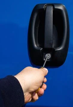 Thief using screwdriver to break into blue car door lock Stock Photos