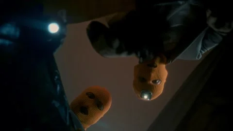 Thieves in masks with flashlights open a black bag with the loot and look inside Stock Footage 312985569