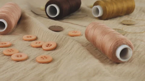 Thin beige cotton jersey, buttons and spools of threads in different shades. Stock Footage 290813472