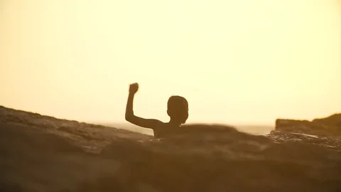 A thin boy climbs a stony ocean beach and runs along it at sunset Stock Footage 89269554