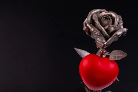 A thin bronze rose made by forging from metal. Red volumetric heart nearby. Stock Photos