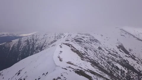 Thin clouds hide mountain peak. Aerial view from drone of snowy ridgeline Video stock 247181022