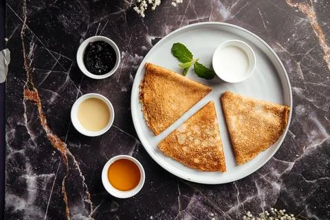 Thin crepes bliny with assorted sauces on marble table Stock Photos